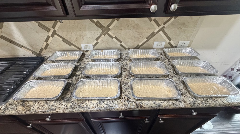 Twelve loaf pans of banana bread batter lined up on a kitchen counter