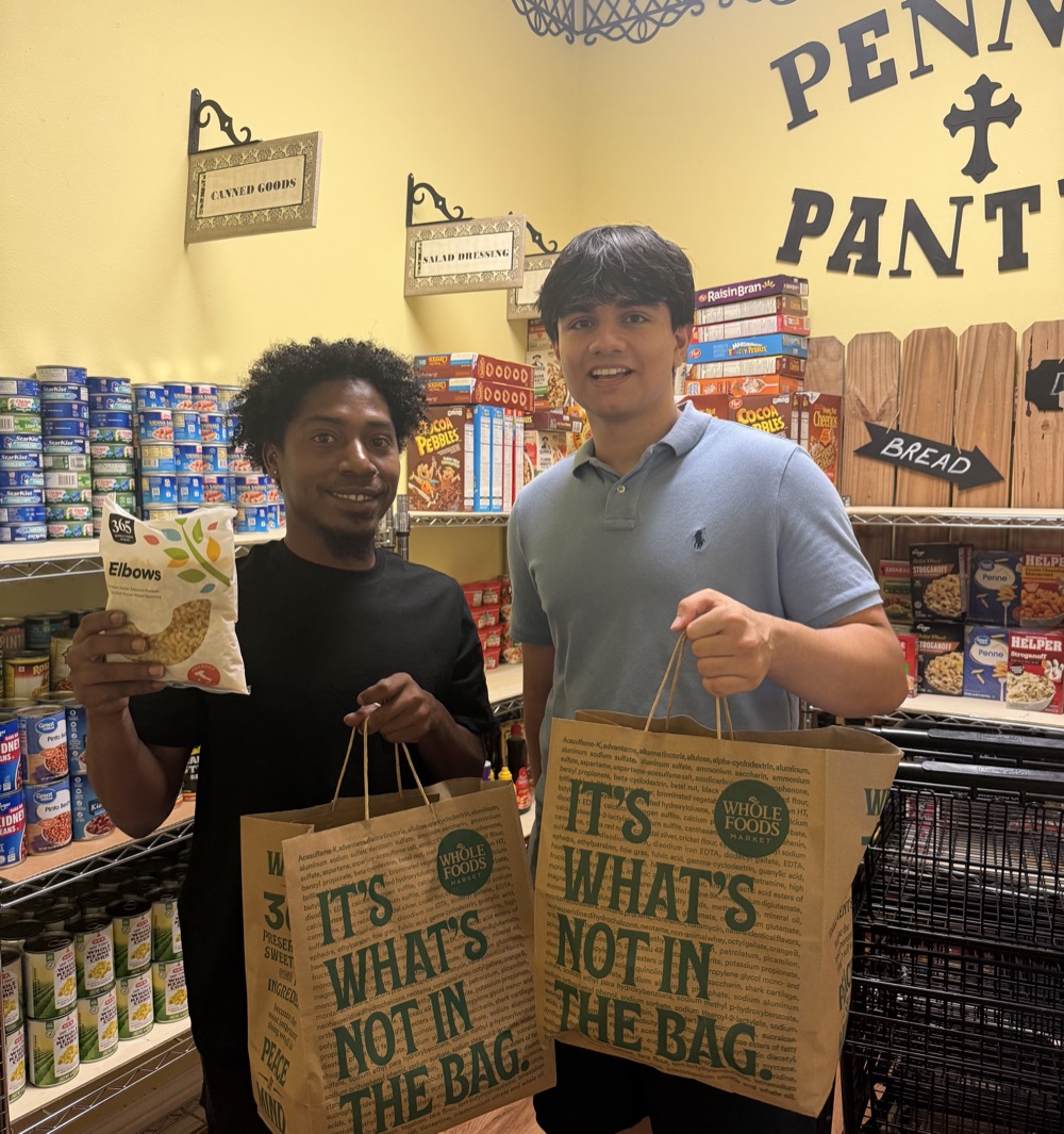 Sid Sharma and a volunteer holding Whole Foods bags of rescued groceries inside a stocked food pantry