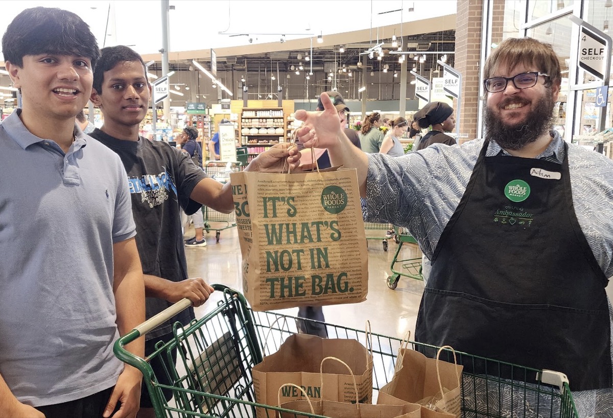 A Whole Foods Market team member handing a donation bag to Sid Sharma and a volunteer with a cart of bags