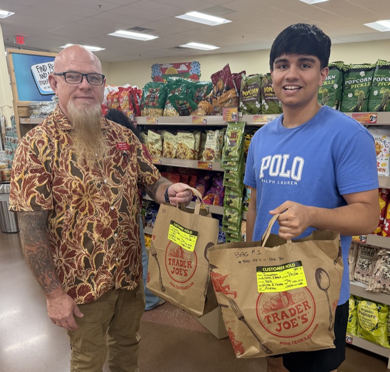 Sid Sharma and a Trader Joe's crew member holding two bags tagged as Waste 2 Taste donations