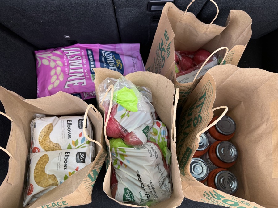 Rescued groceries in a car trunk: pasta, rice, potatoes, apples, and canned goods
